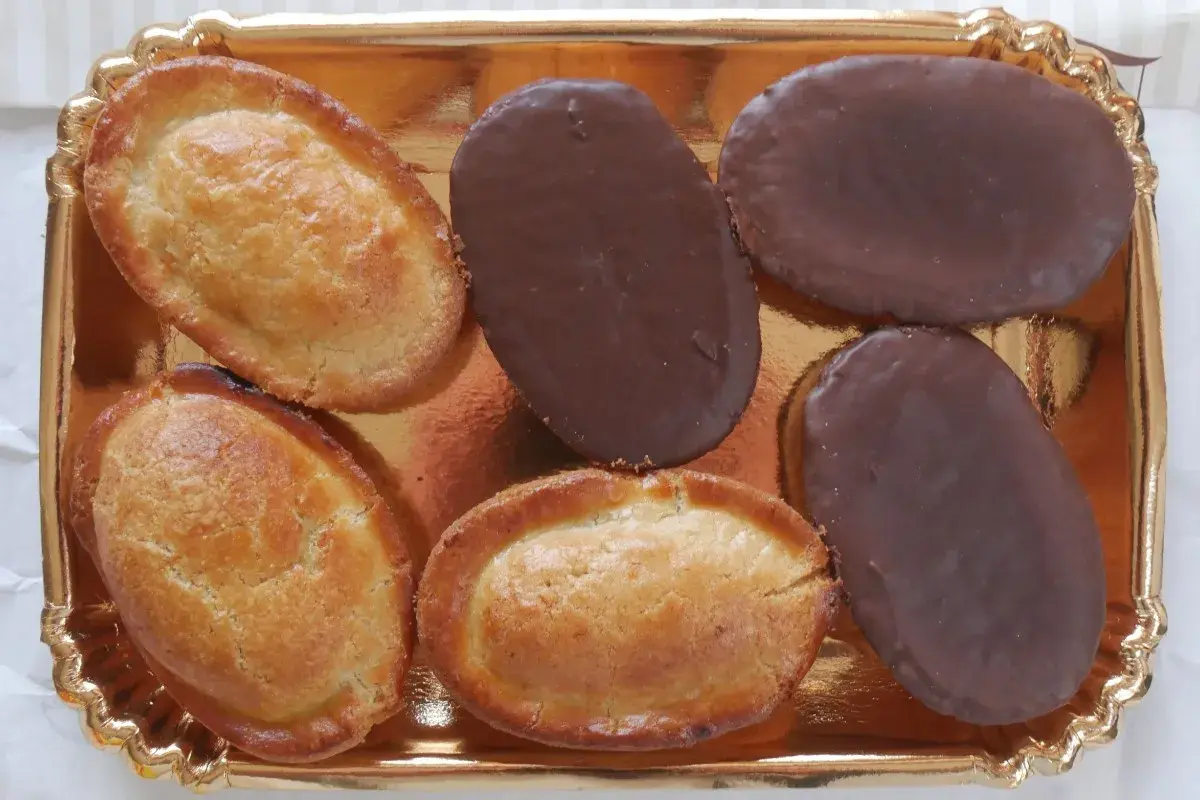 Sei fruttoni leccesi, tre ricoperti di cioccolato fondente e tre dorati, disposti su un vassoio dorato.