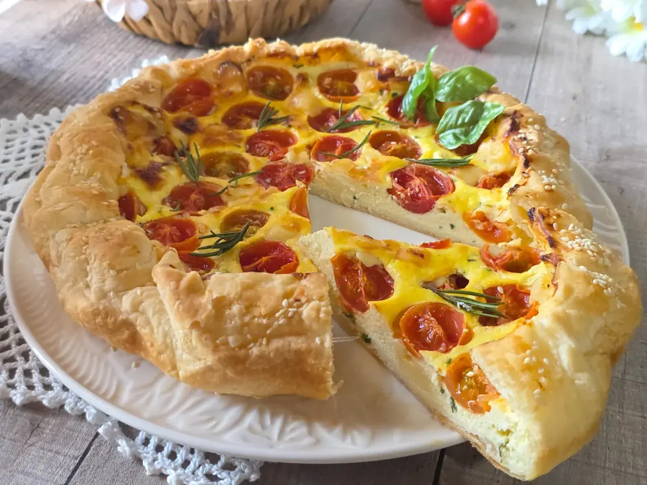 Une quiche ricotta aux tomates cerises et romarin, garnie de graines de sésame, sur une assiette blanche.
