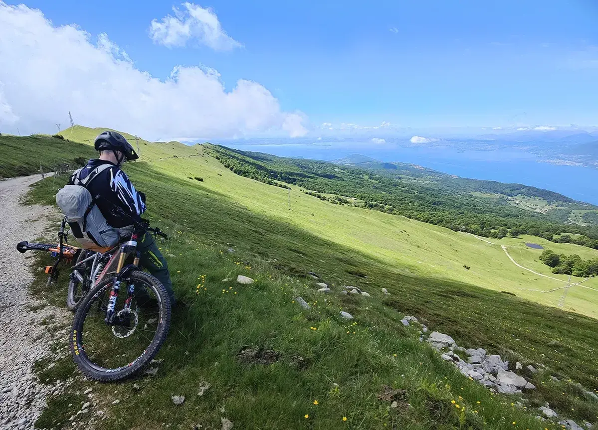 Ciclista con mountain bike ammira il panorama del lago di Garda dal Monte Baldo.
