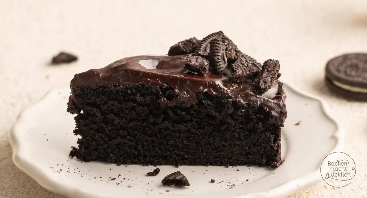 Ein Stück saftiger Oreo Kuchen mit glänzender Schokoladenglasur und zerbröselten Keksen obendrauf.