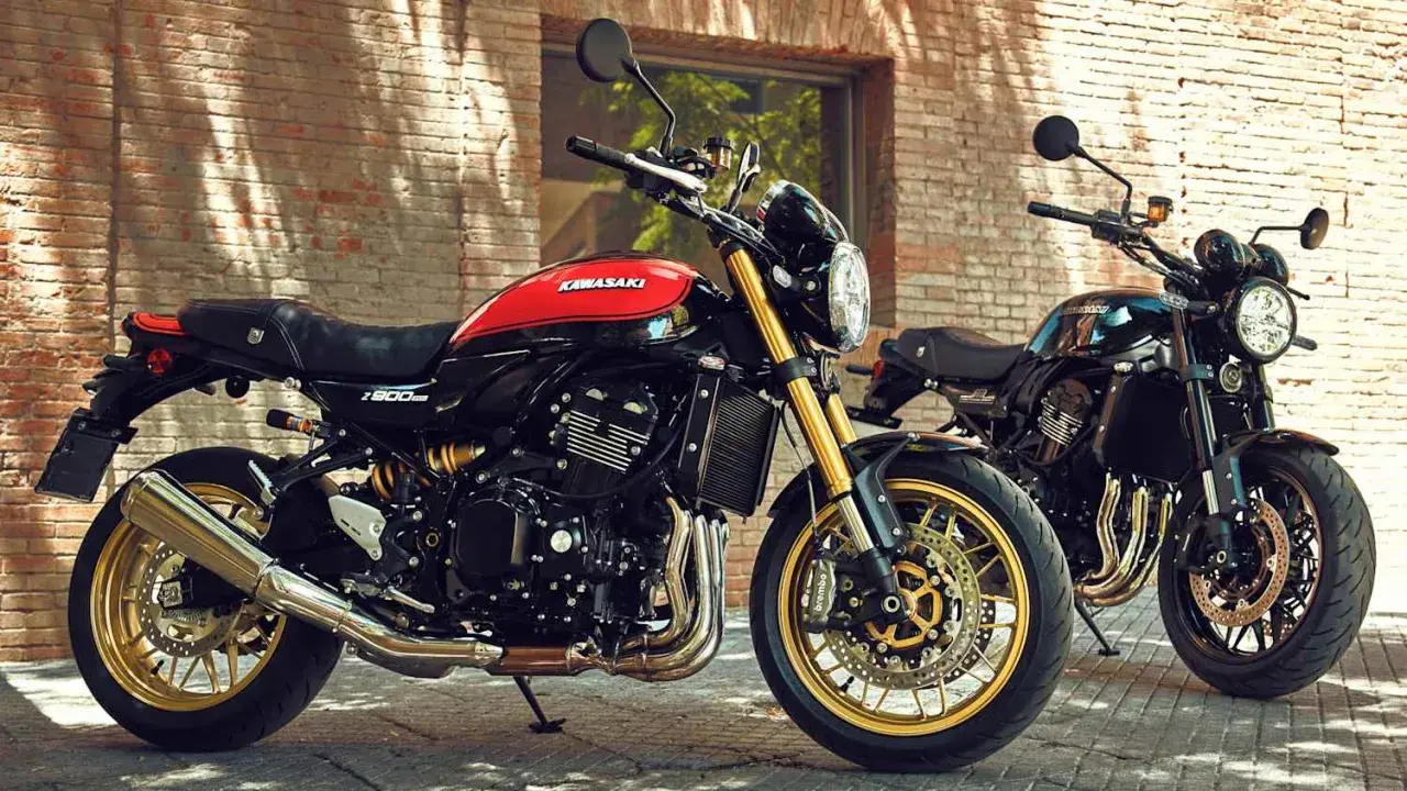 Zwei Kawasaki Z900RS, ein retro Motorrad in Schwarz-Rot, und ein weiteres in Schwarz, stehen vor einer Ziegelwand.