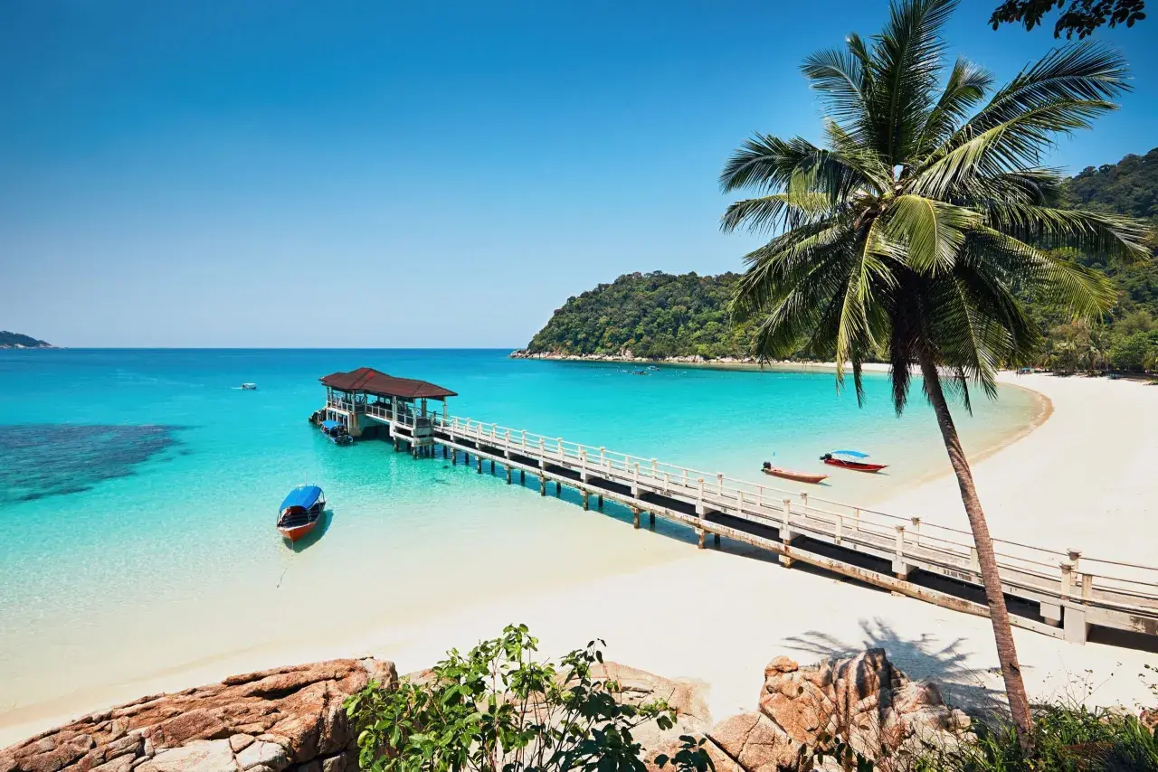 Traumhaftes Malaysia Wetter im Juli: Türkisblaues Meer, weiße Sandstrände, Palmen und eine Anlegestelle mit Booten. Perfekt für einen Urlaub!