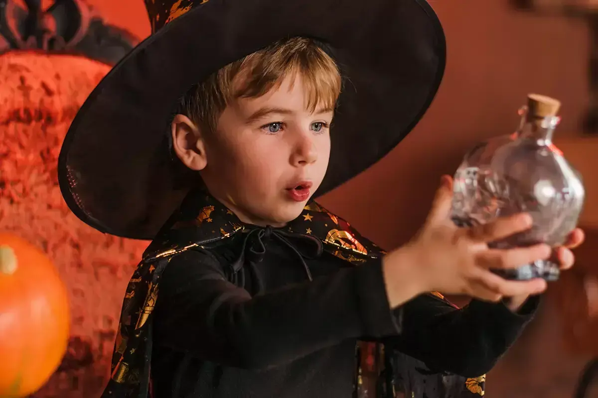 Niño mago con sombrero y capa, sosteniendo una botella con forma de calavera. ¡Perfecto para trucos de magia para niños de 3 a 6 años!
