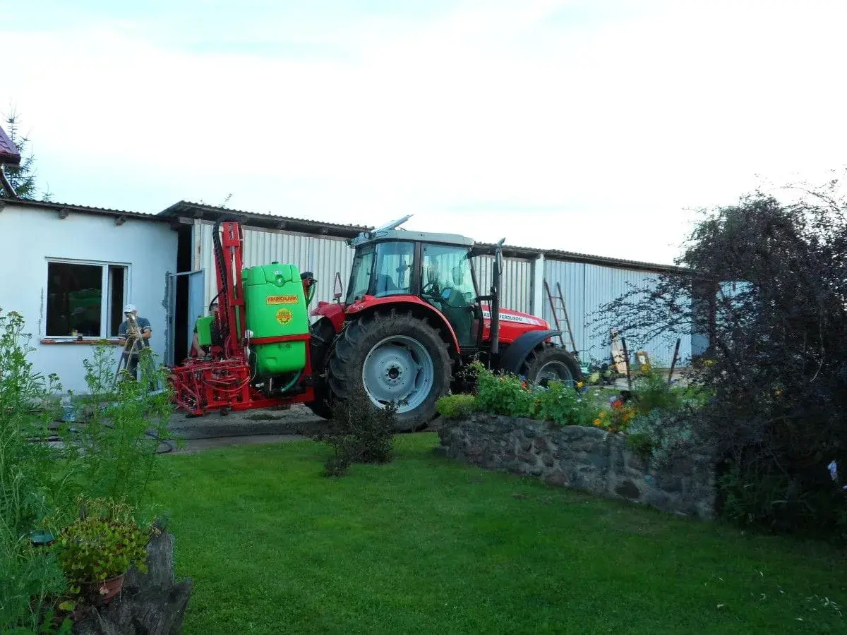 Czerwony traktor z opryskiwaczem czeka na deszcz. Rolnik przygotowuje sprzęt, by zdążyć przed ulewą.
