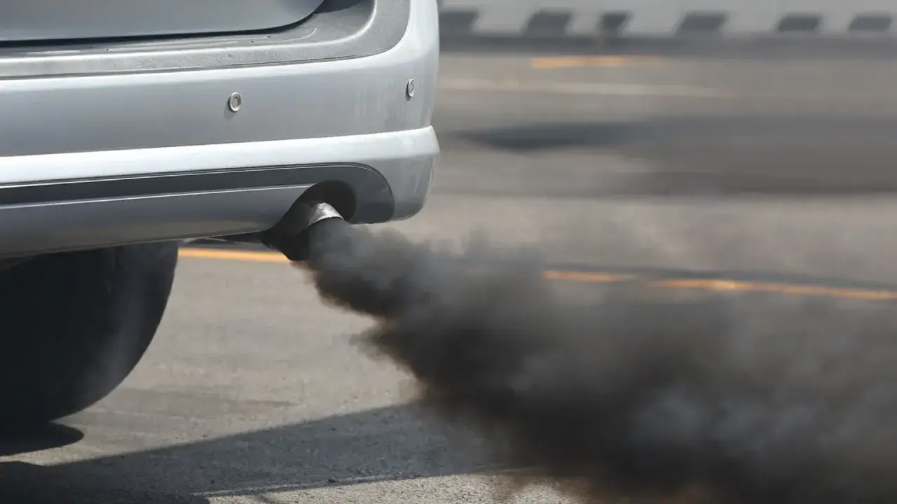 Humo negro al arrancar diésel, una nube densa sale del tubo de escape de un coche plateado.