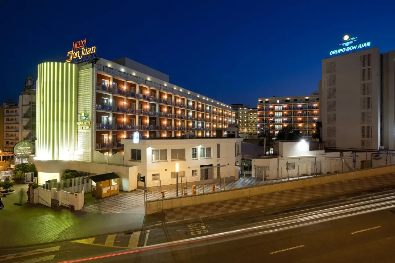 Hotel Don Juan Resort nocą, z neonowym oświetleniem i widokiem na wiele balkonów.