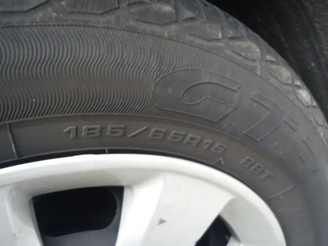 Gros plan sur un pneu rechapé avec inscription 185/65R15. La jante est visible en bas.