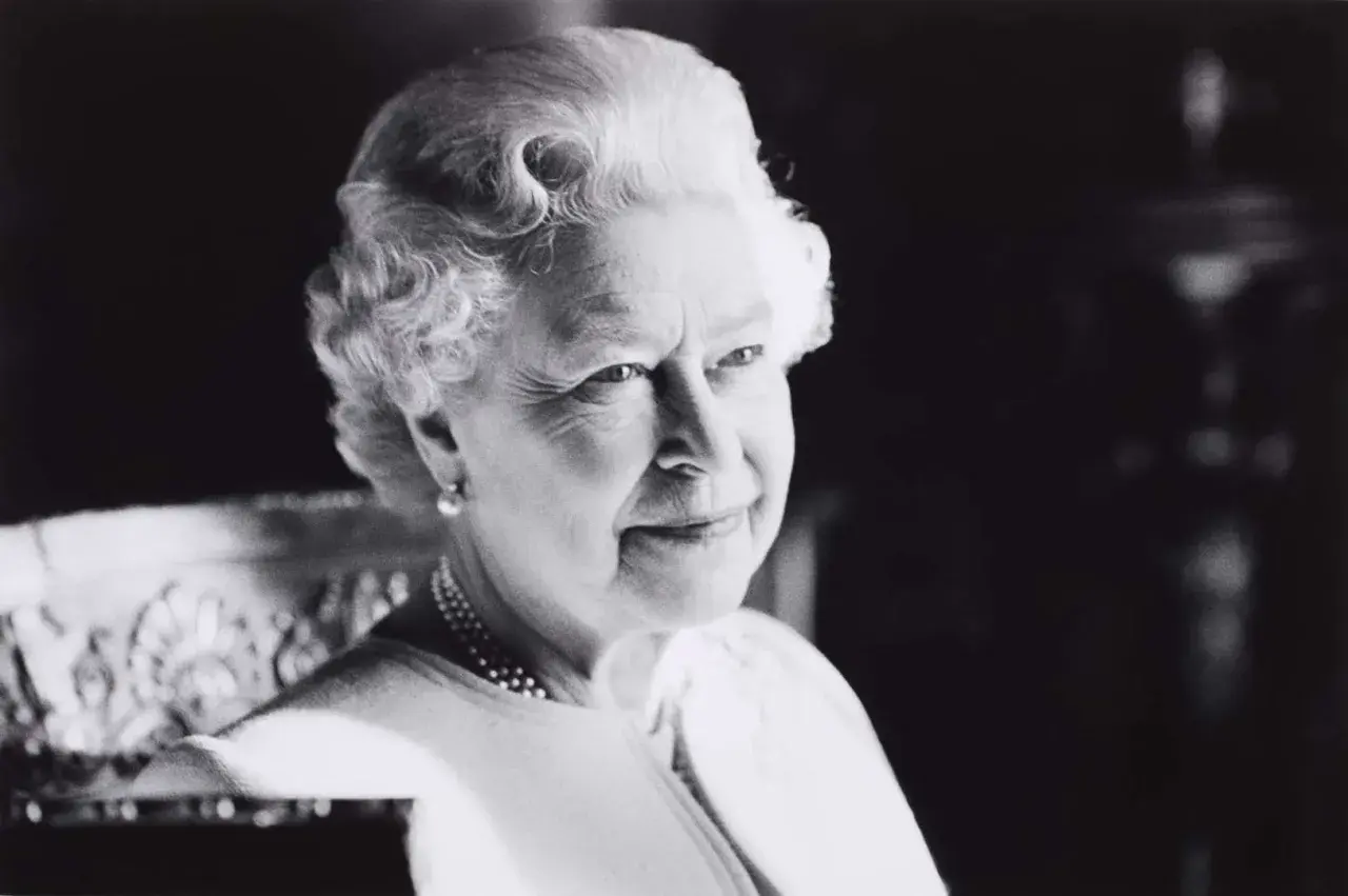 A classic Sutherland portrait of the Queen, her gaze thoughtful, adorned with pearls and a subtle smile.