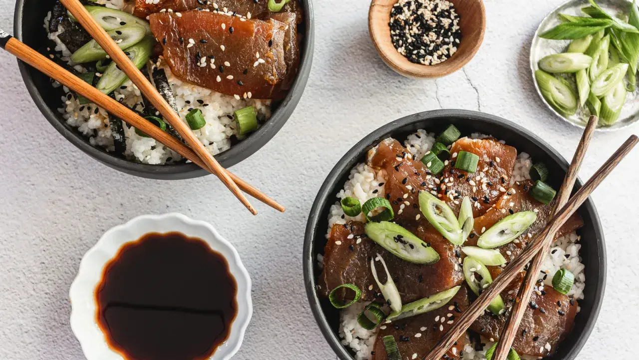 Two bowls of delicious tuna rice don, garnished with sesame seeds and green onions, are ready to be enjoyed with chopsticks.