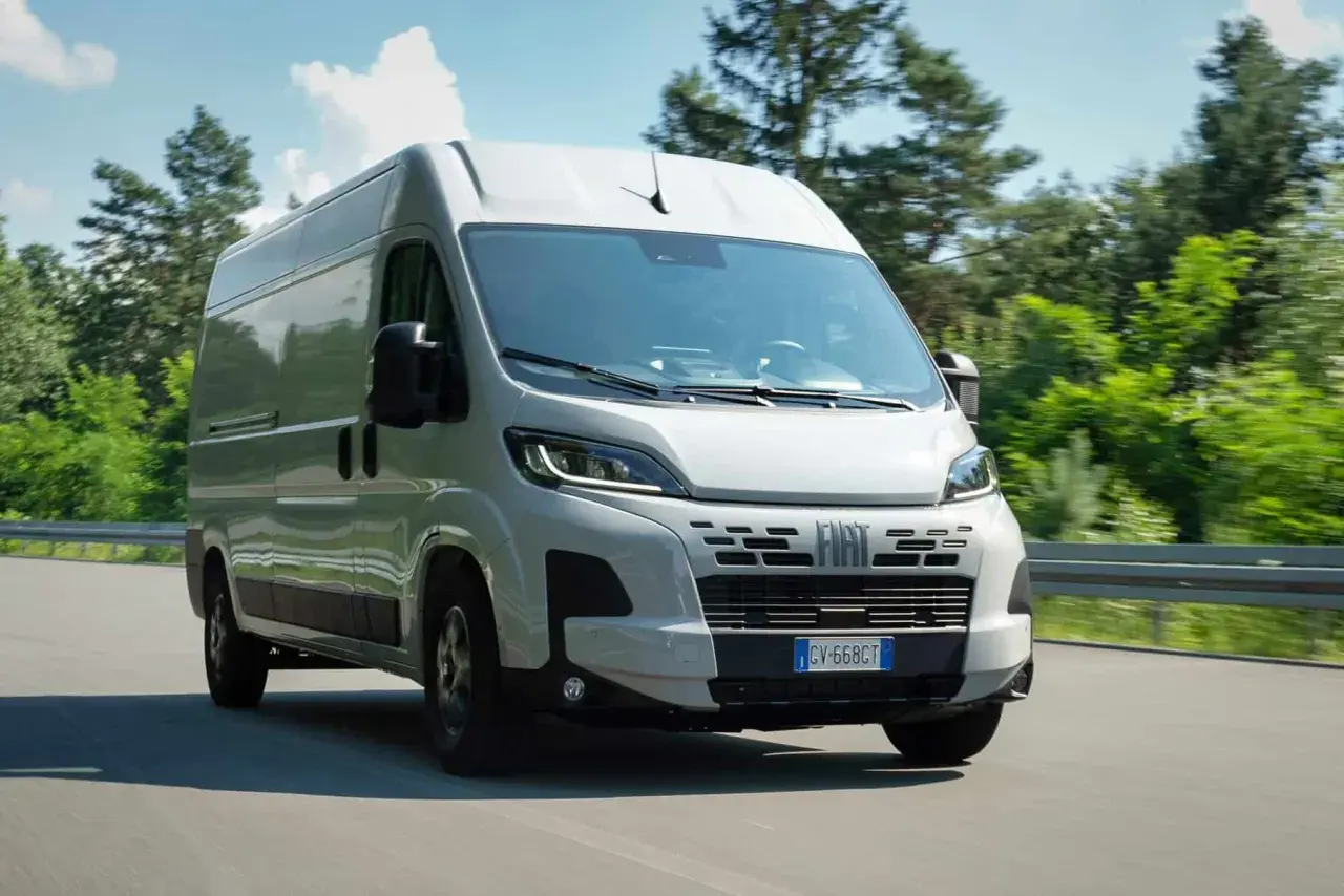 Un Fiat Ducato 2.2 Multijet 140 CV AdBlue blanc roule sur une route bordée d'arbres verts.