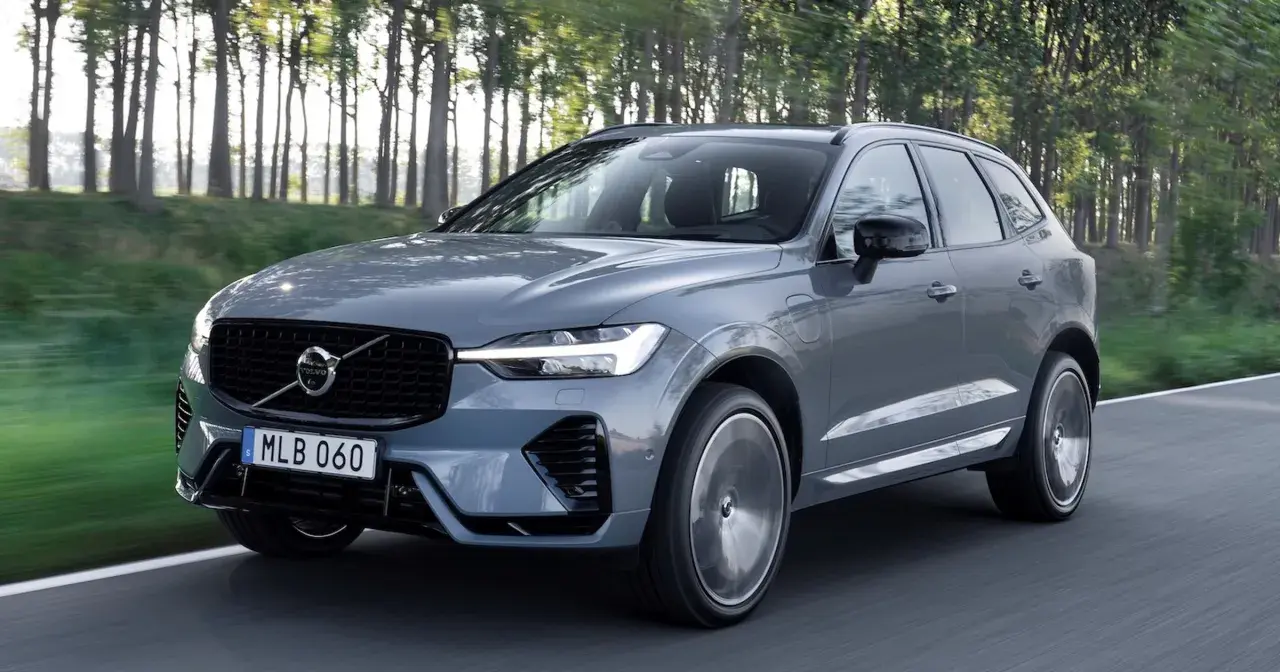 Szary Volvo XC60 z napędem hybrydowym, poruszający się po leśnej drodze. Dostępne różne silniki.