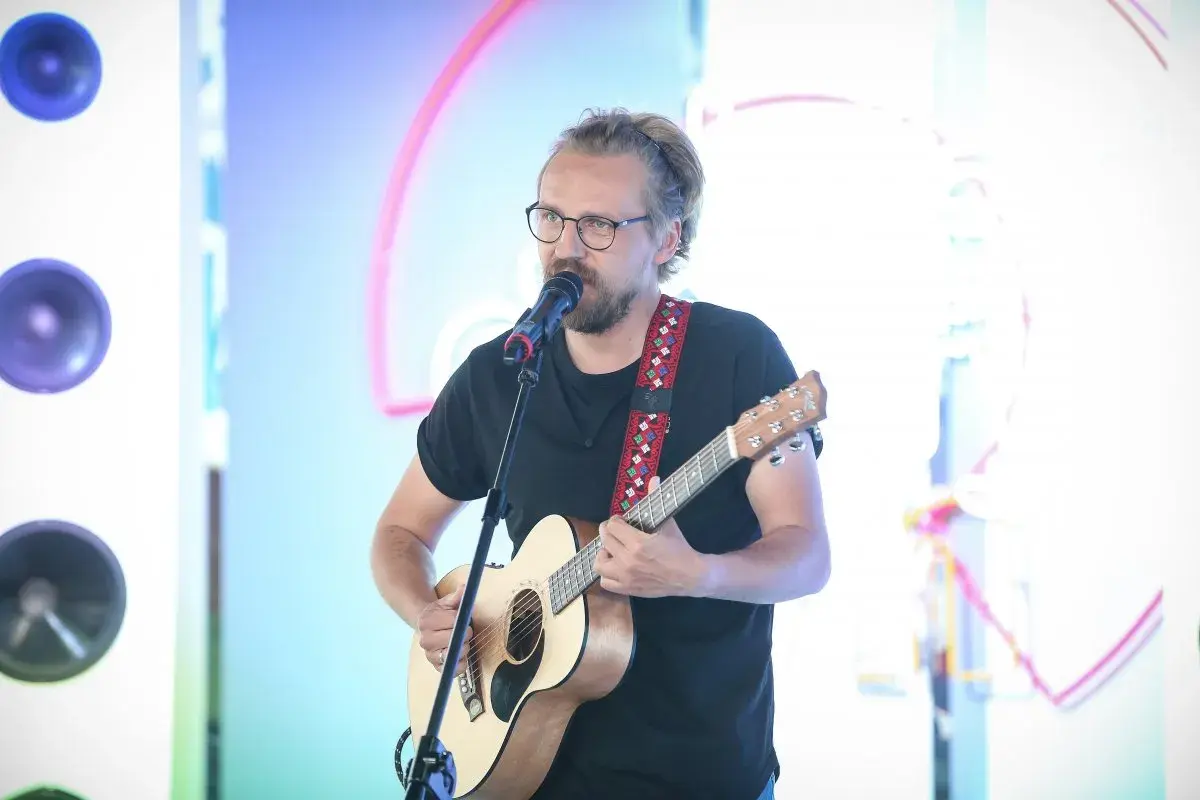 Mężczyzna w okularach gra na gitarze i śpiewa do mikrofonu. Chciałbyś, żeby ktoś powiedział mu "weź się przytul".