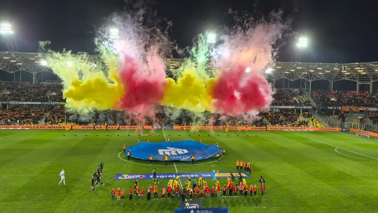 Oprawa meczu Korona Kielce – Jagiellonia Białystok. Piłkarze wychodzą na murawę w otoczeniu gęstego dymu w barwach żółto-czerwonych.