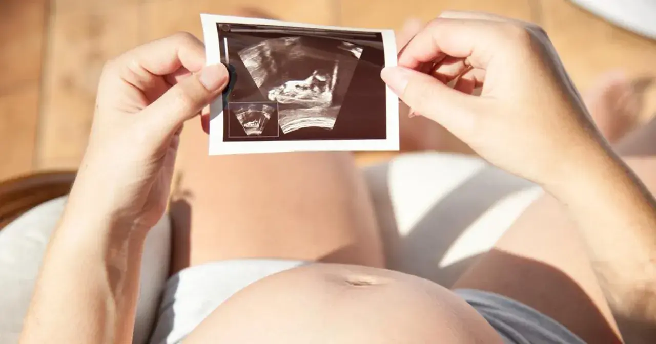 Kobieta trzyma zdjęcie USG, na którym widać zarodek. To nie lewatywa, a cud życia.