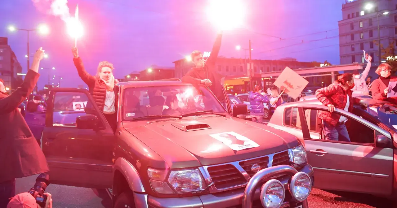 Ludzie z flarami przy samochodach, protestują. Tekst po polsku "Bella Ciao" może być na transparentach.
