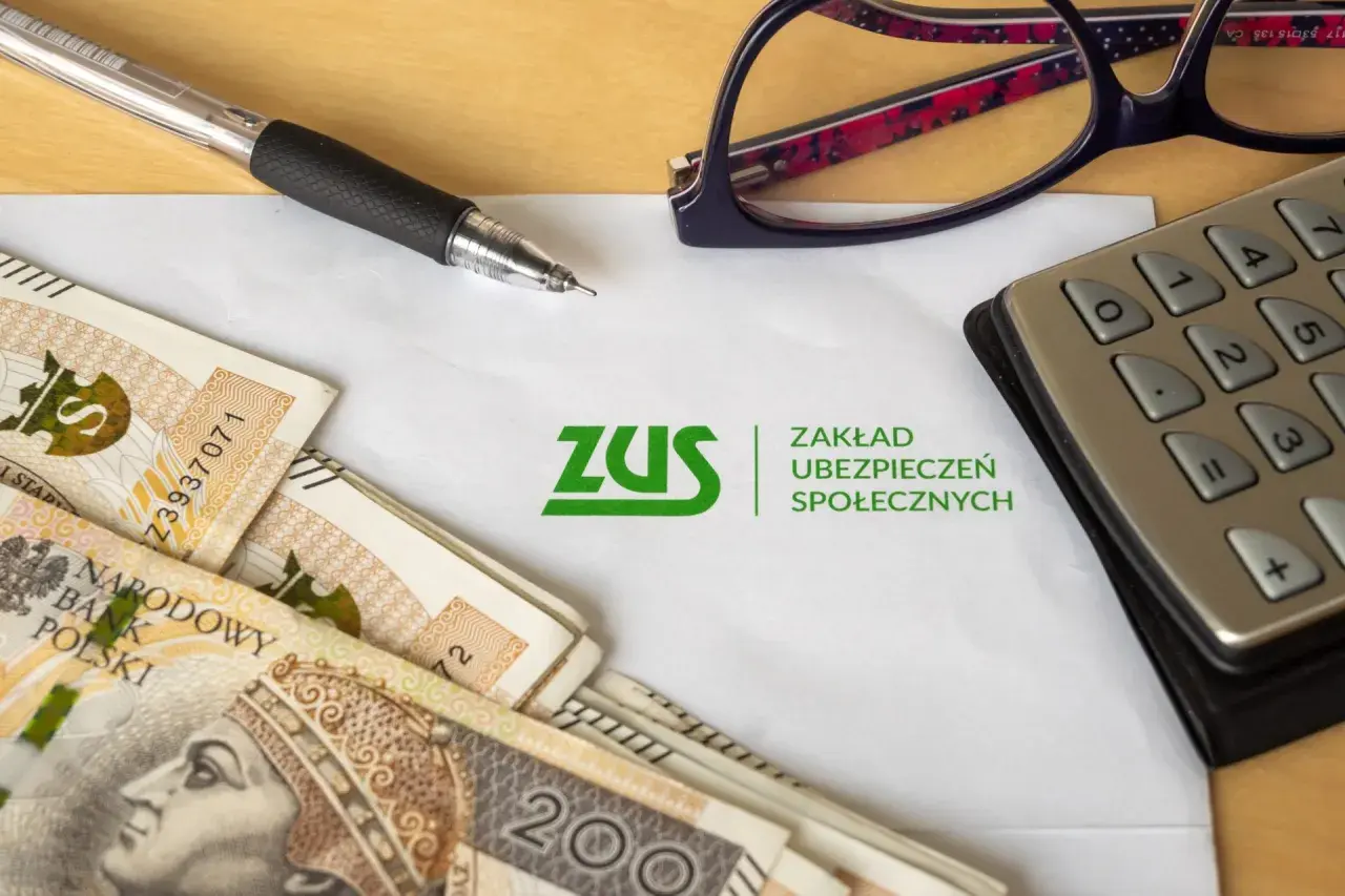 Pieniądze, długopis, kalkulator i okulary leżą obok logo ZUS. Czy to wszystko, co musisz wiedzieć o smishingu?