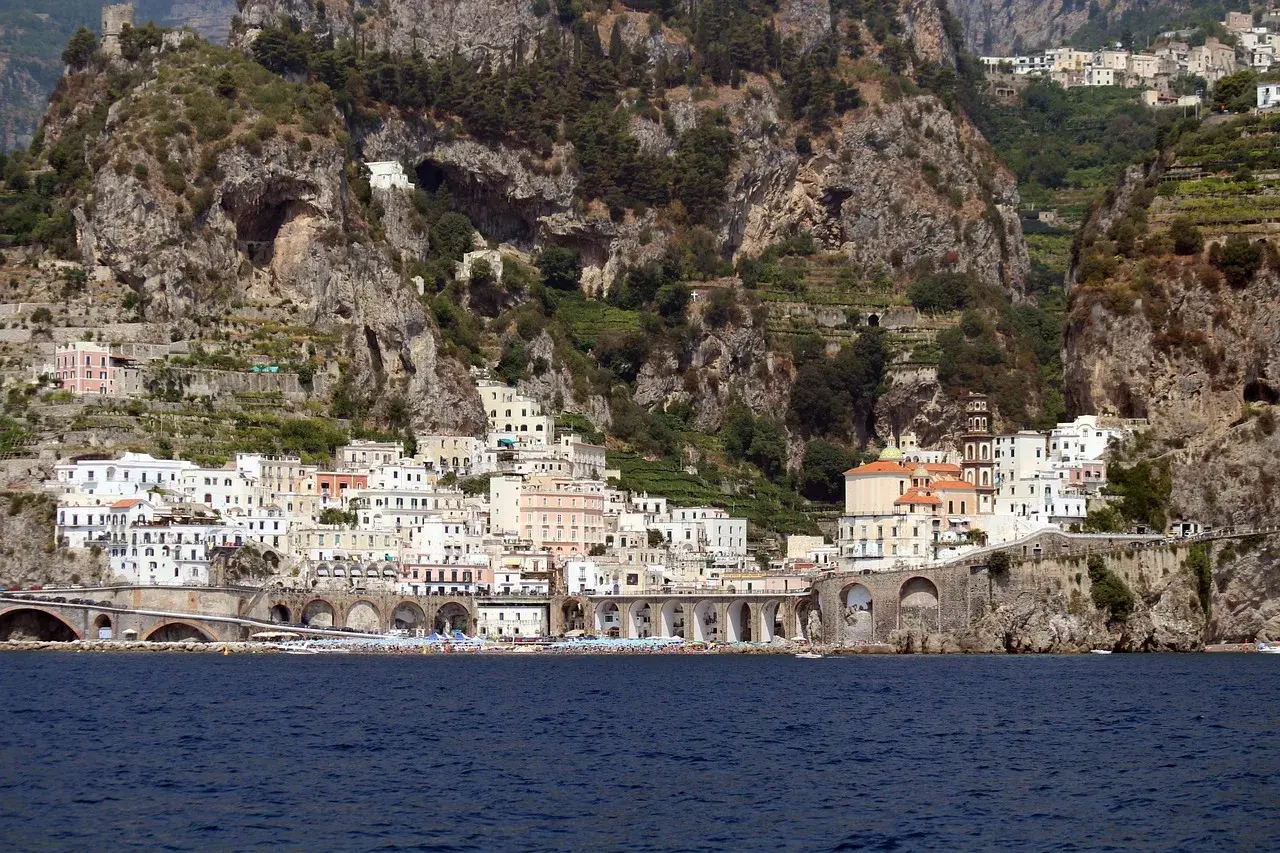 Atrani beach club nestled below dramatic cliffs, with colorful buildings cascading down to the sea.