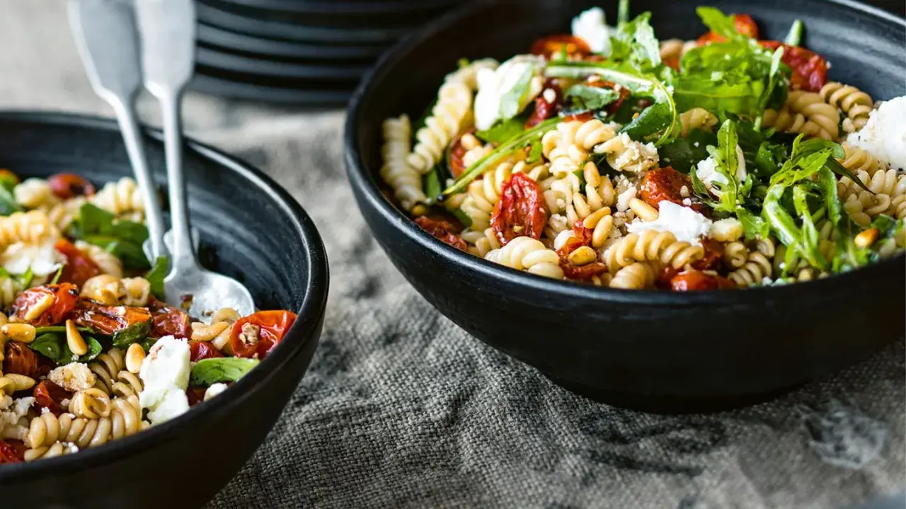 Zwei Schalen mit einem köstlichen nudelsalat mit getrockneten tomaten, Pinienkernen und Rucola, garniert mit Feta.