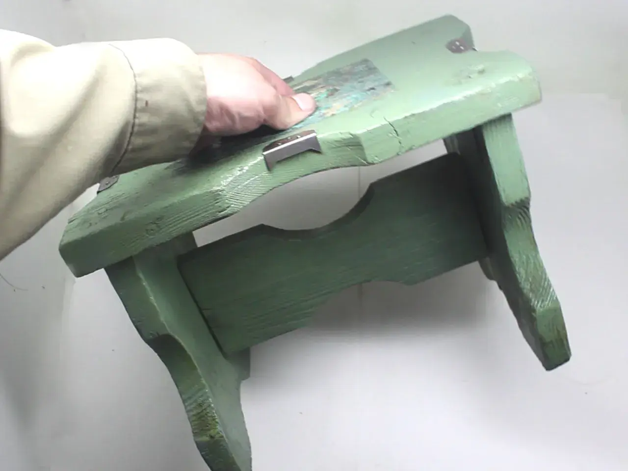 Mano che tiene uno sgabello di legno verde, pronto per verniciare con bomboletta spray.