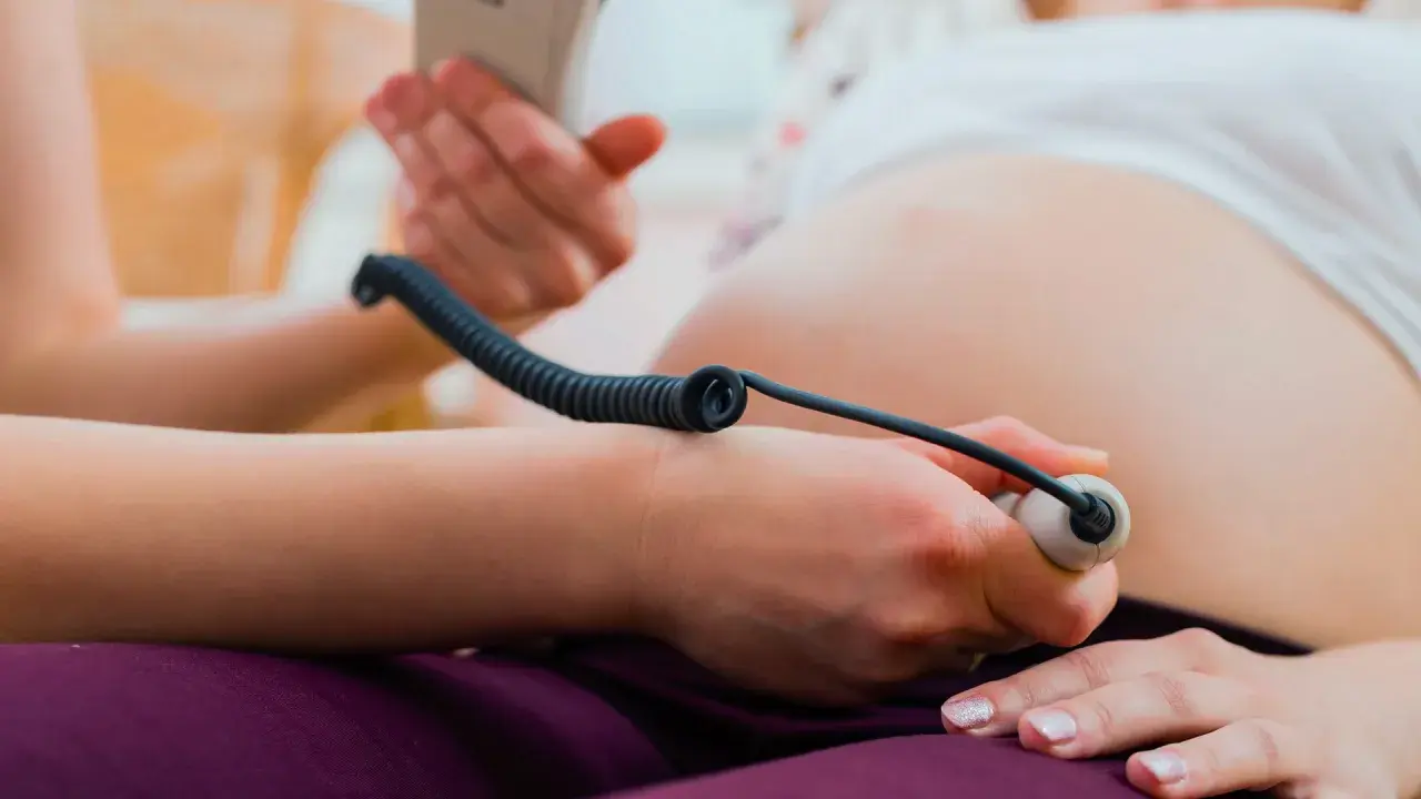 Gravid kvinna får sitt foster lyssnat på med doppler. Vårdgivaren håller instrumentet mot magen.