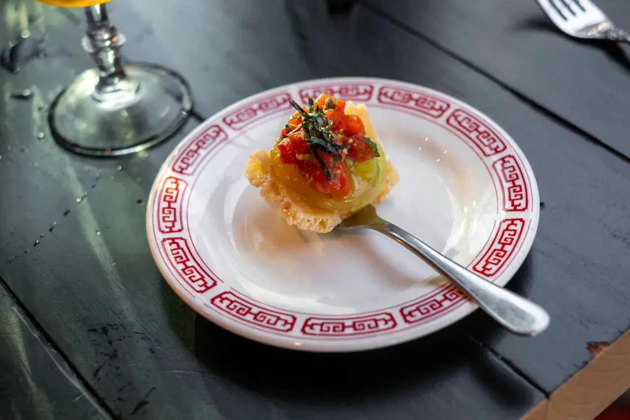 Wykwintny amuse bouche z awokado i pomidorkami na chrupiącym spodzie, podany na talerzyku z czerwonym wzorem.
