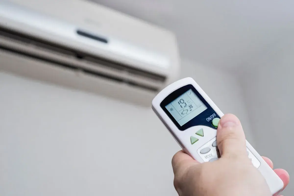Mando a distancia ajustando la temperatura ideal aire acondicionado para ahorrar energía. Se ve el aire acondicionado y la mano con el control.