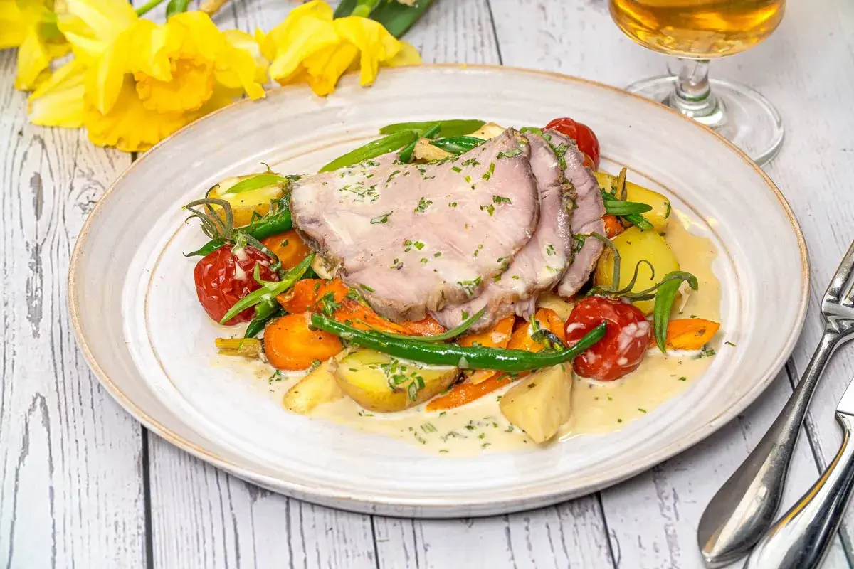 Skinkstek i ugn serverad med rotfrukter, gröna bönor och en krämig sås. En härlig vårmåltid.