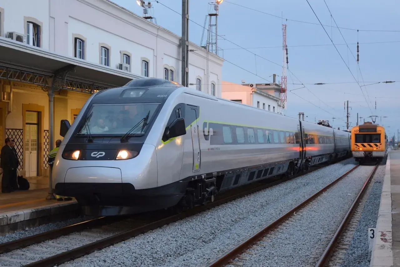 Tren moderno plateado y otro amarillo en estación, listos para el viaje de Lisboa a Oporto.