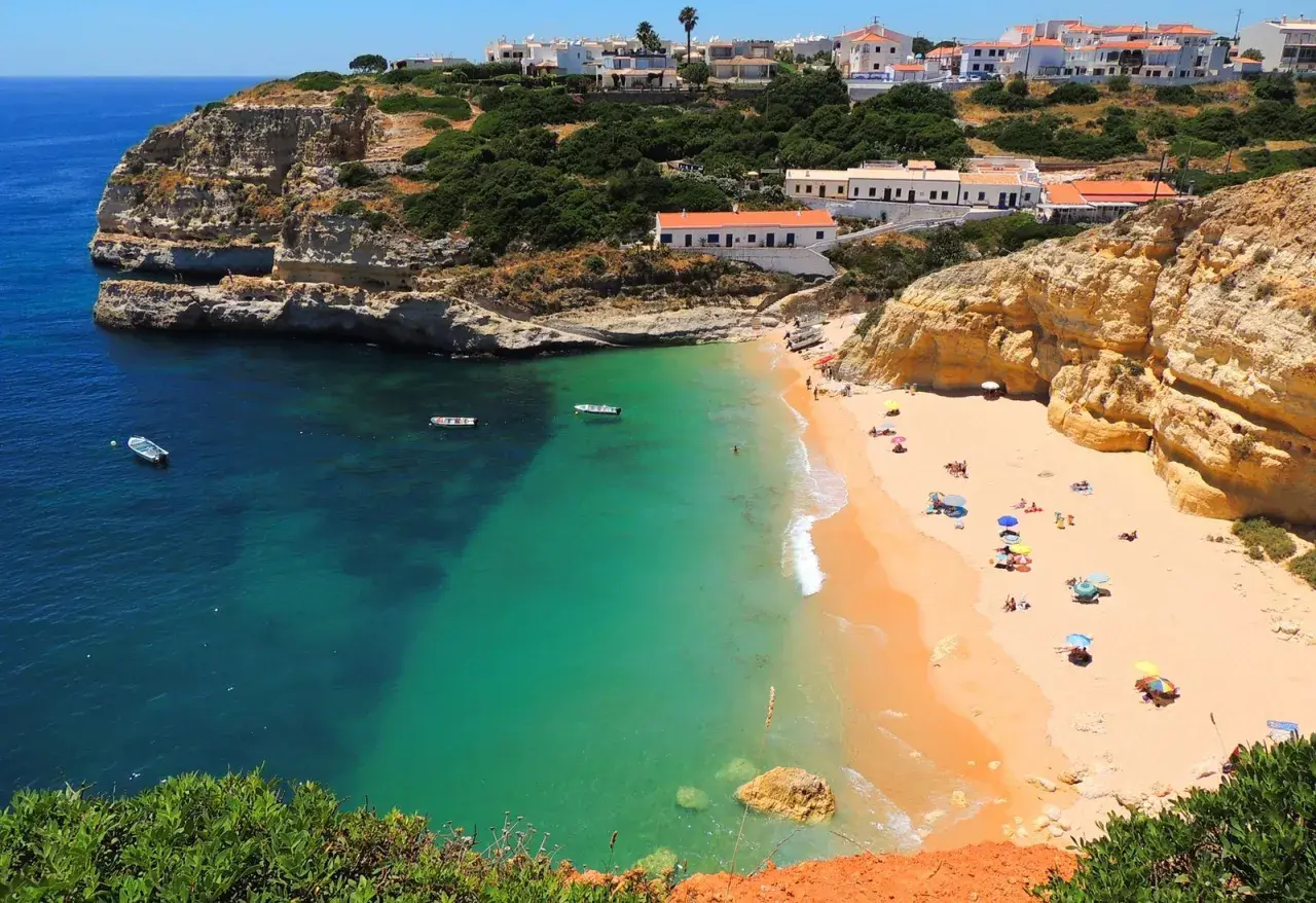 Playa dorada con aguas turquesas y acantilados, ideal para tu plan de algarve en 6 dias. Casas blancas coronan la colina.