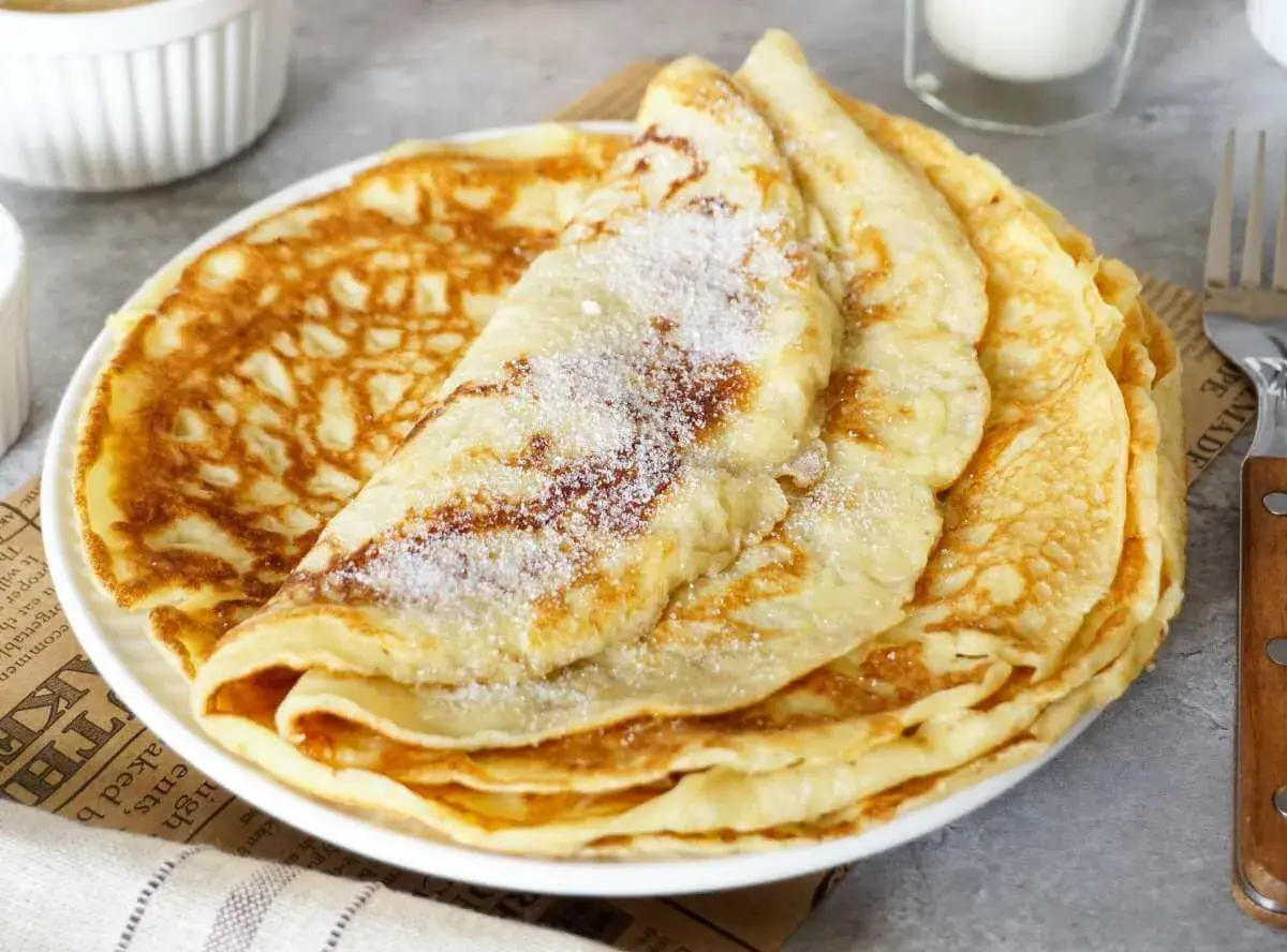 Ein Stapel goldbrauner Pfannkuchen, bestreut mit Zucker. Ein einfaches Pfannkuchen Rezept für jeden Tag.