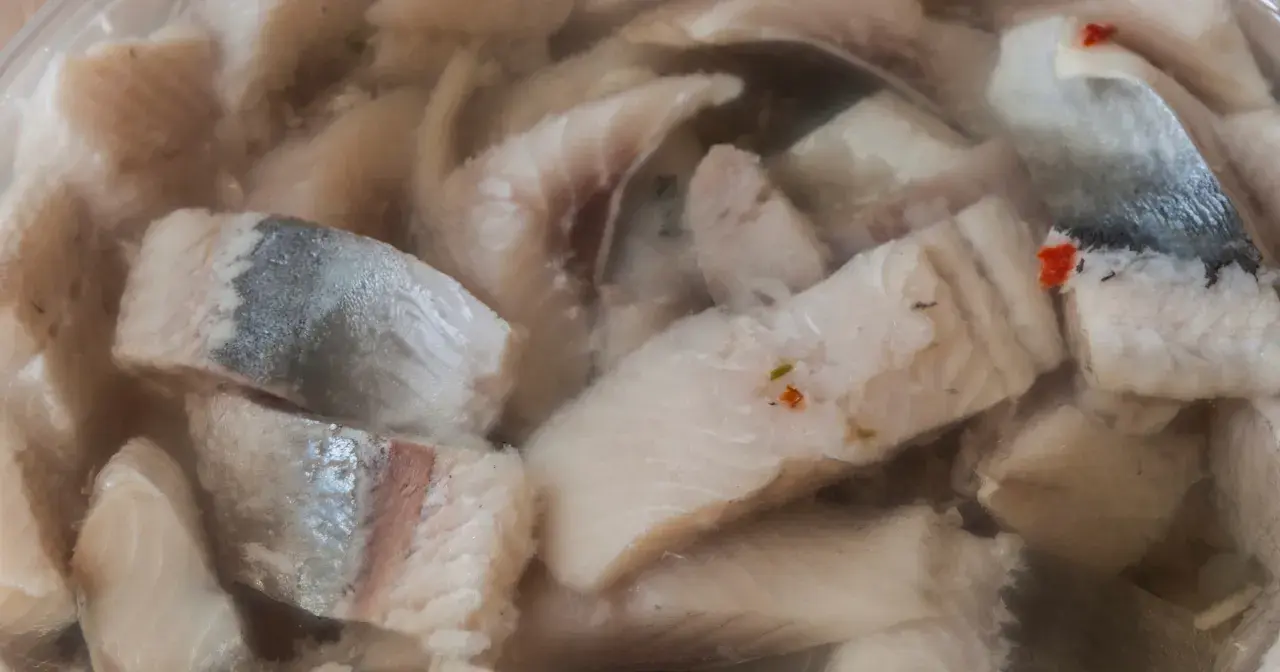 Kawałki kiszonych śledzi w zalewie, niektóre z drobinkami przypraw.