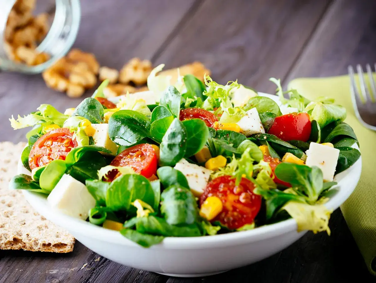 Ein bunter gemischter Salat mit Tomaten, Mais und Feta-Käse, serviert in einer weißen Schüssel auf einem Holztisch.