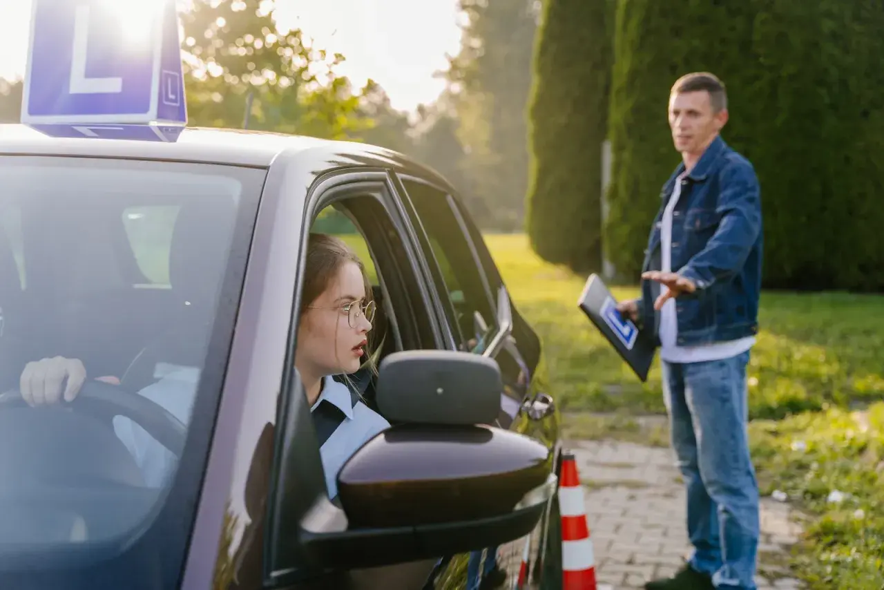 Młoda kursantka za kierownicą samochodu z literą "L", instruktor obok z tabliczką. Czy kurs na prawo jazdy przepada?