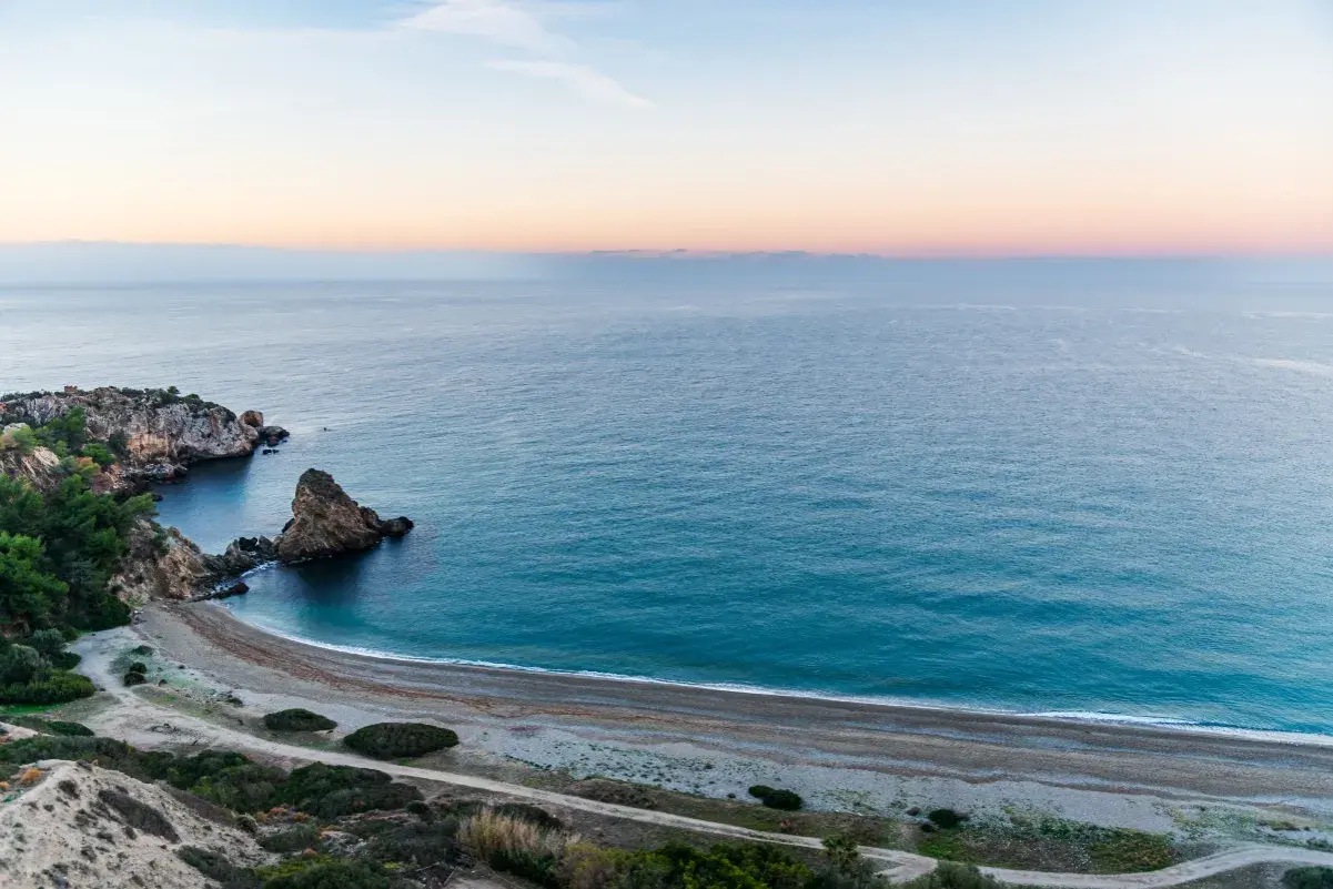 Vista aérea de una cala rocosa y una playa de guijarros en las playas de Málaga al amanecer.