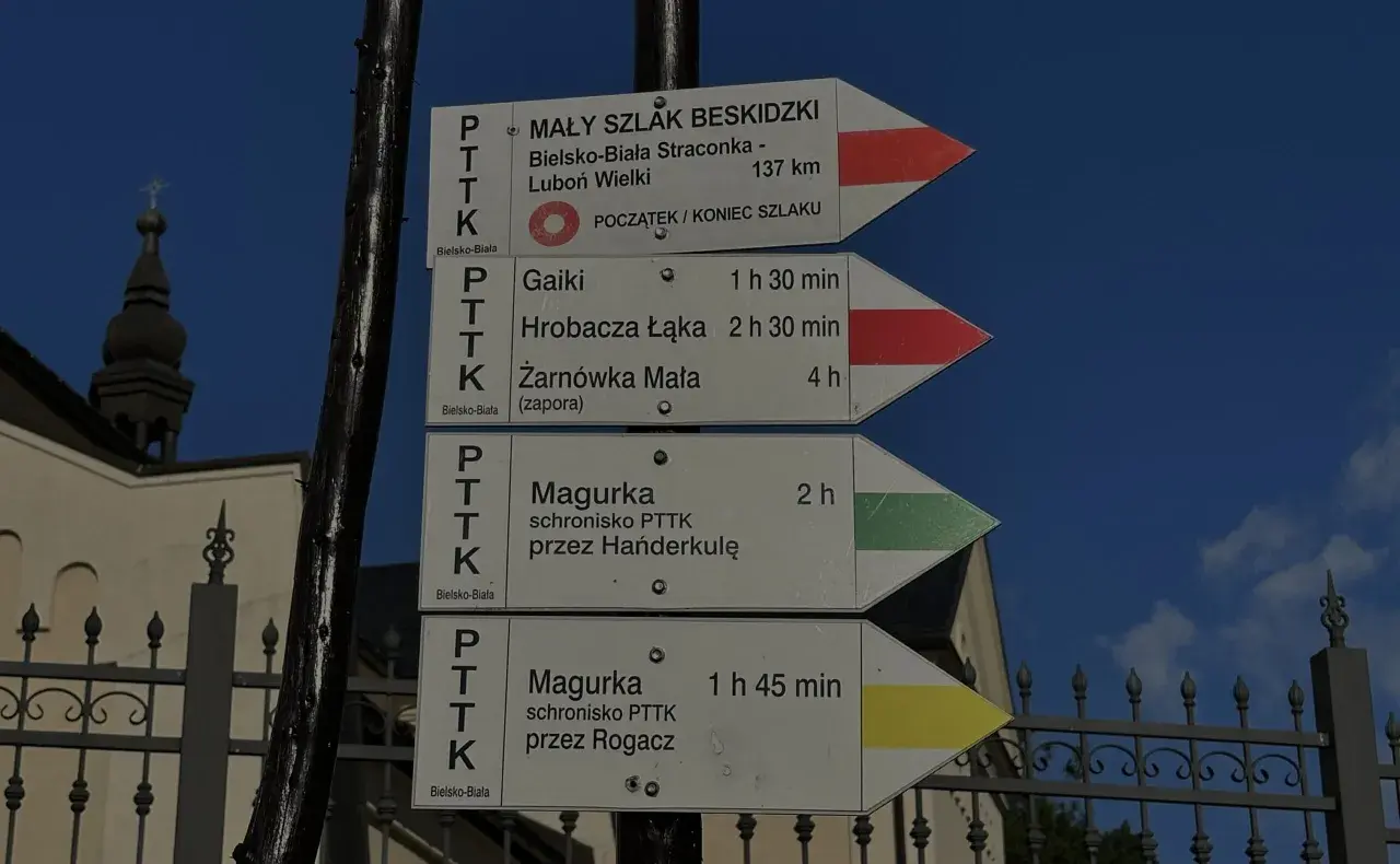 Znaki szlaku turystycznego, w tym czerwony szlak, wskazują drogę do Magurki, Gaików i innych beskidzkich celów.
