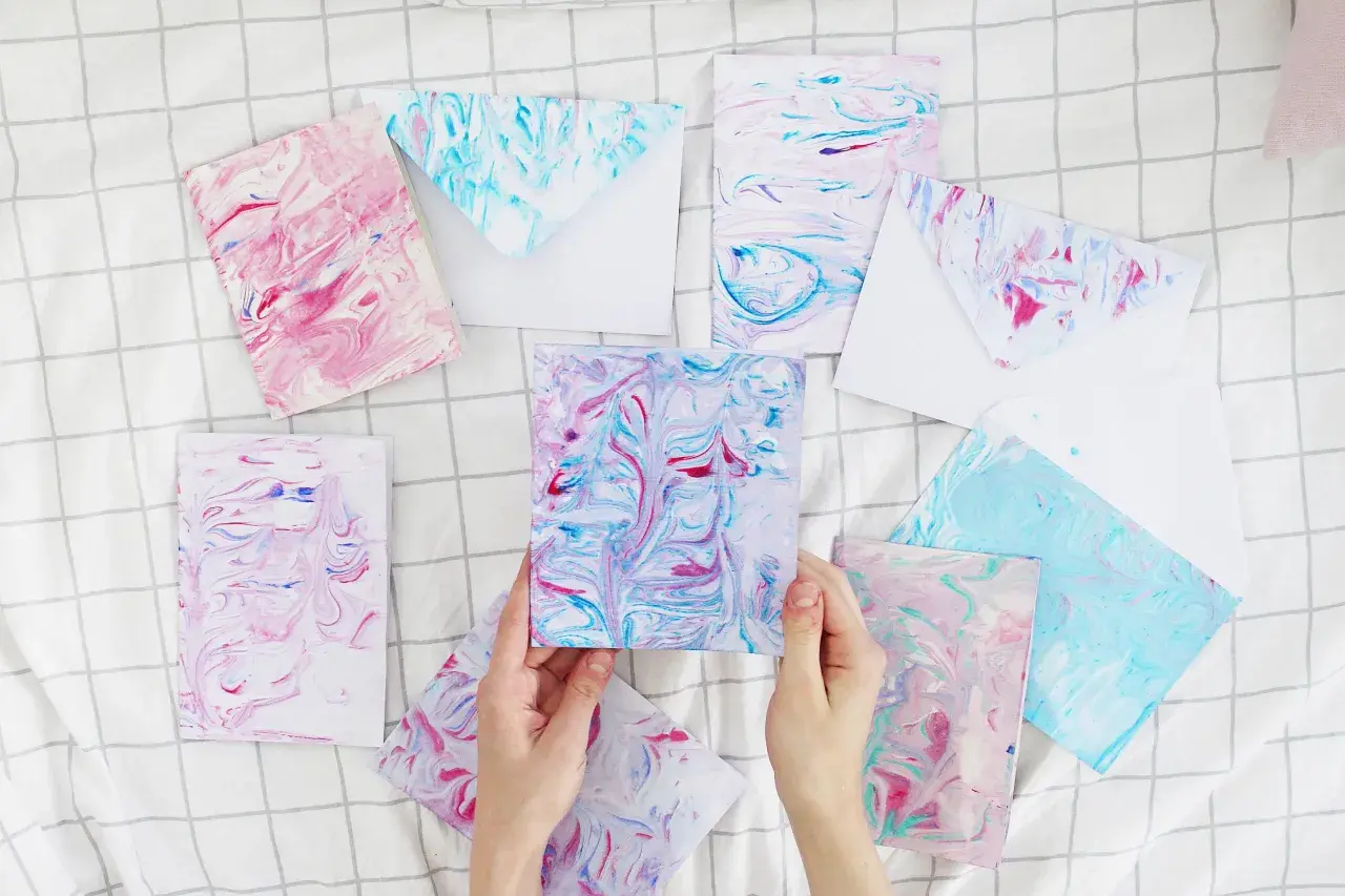Bunte Karten und Umschläge mit Marmorierungsmuster, die an fließendes Wasser erinnern. Papier marmorieren ist eine kreative Technik.