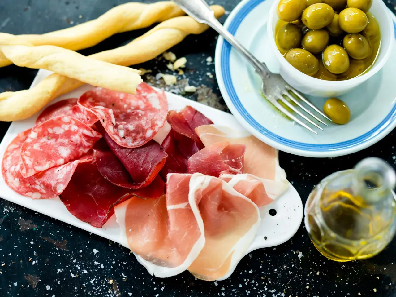 En härlig italiensk tapasbricka med salami, prosciutto, grissini, oliver och olivolja. Perfekt för en mysig kväll.