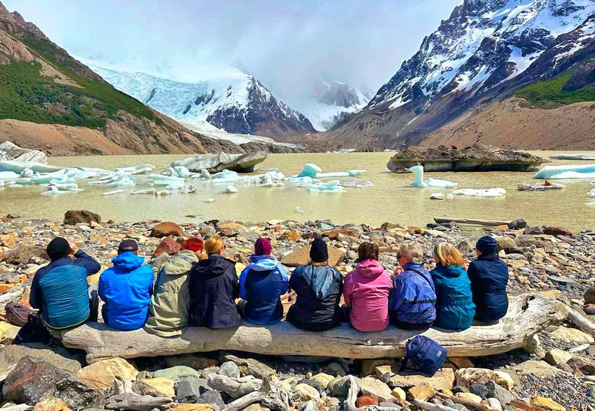 Gruppe sitzt auf Baumstamm vor Gletschersee mit Eisbergen. Tolle Eberhardt Travel Erfahrungen in Patagonien.