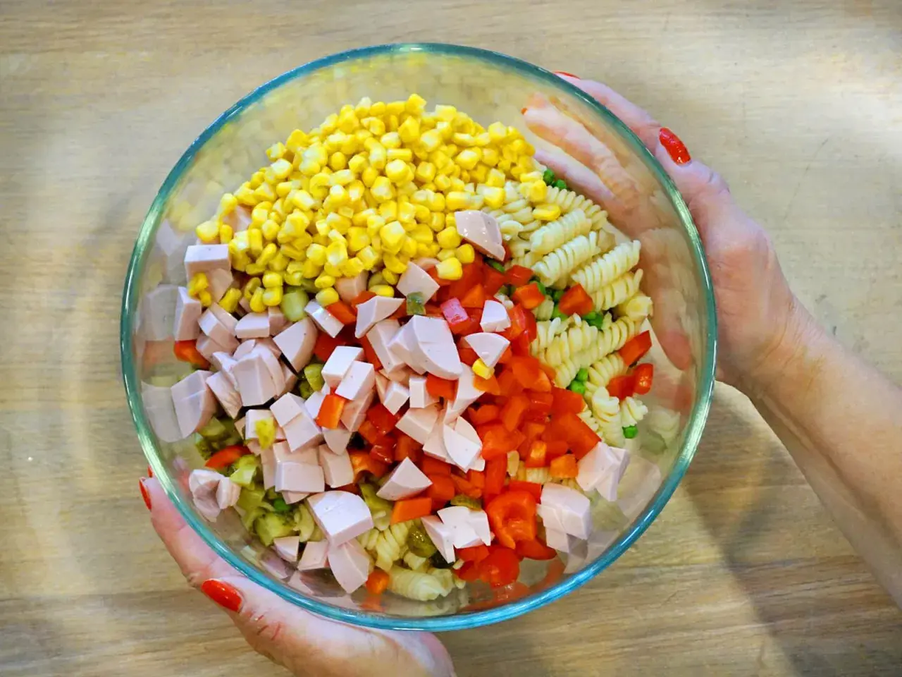 Bunte Zutaten für ein leckeres Nudelsalat Rezept: Mais, Paprika, Wurstwürfel, Erbsen und Spiralnudeln in einer Glasschüssel.