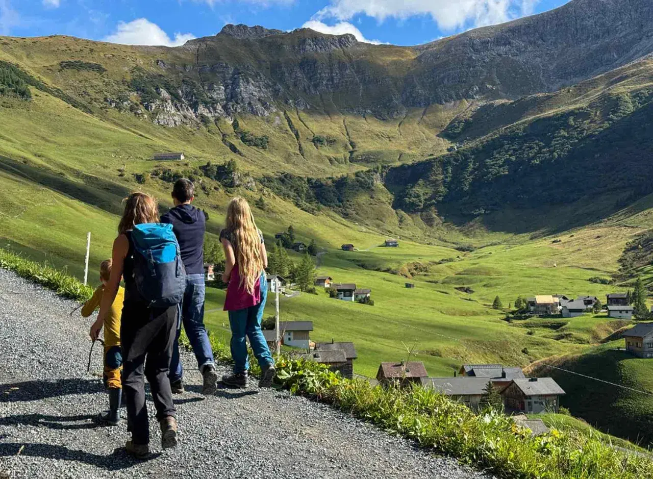 Familie genießt das Liechtenstein wandern in den Alpen. Grüne Hänge, kleine Häuser und ein majestätischer Berg im Hintergrund.