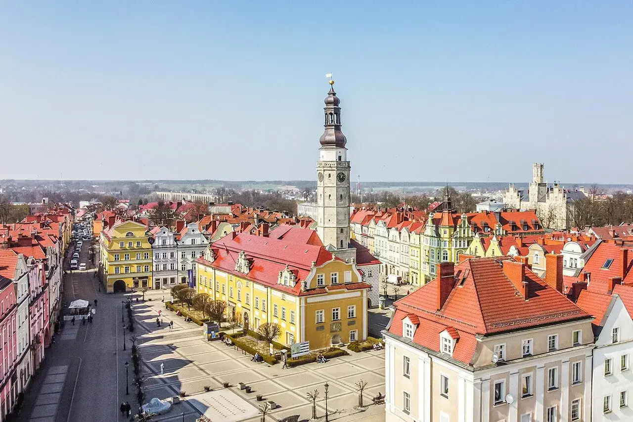 Widok z góry na rynek w Bolesławcu. Dominują kolorowe kamienice z czerwonymi dachami i wysoka wieża ratuszowa.