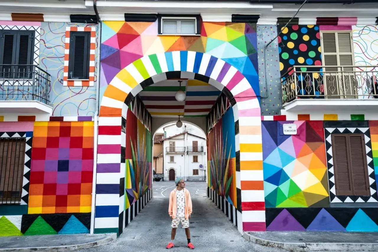Un uomo in piedi sotto un arco colorato, un'esplosione di arte urbana che celebra l'Italia, patria della bellezza.
