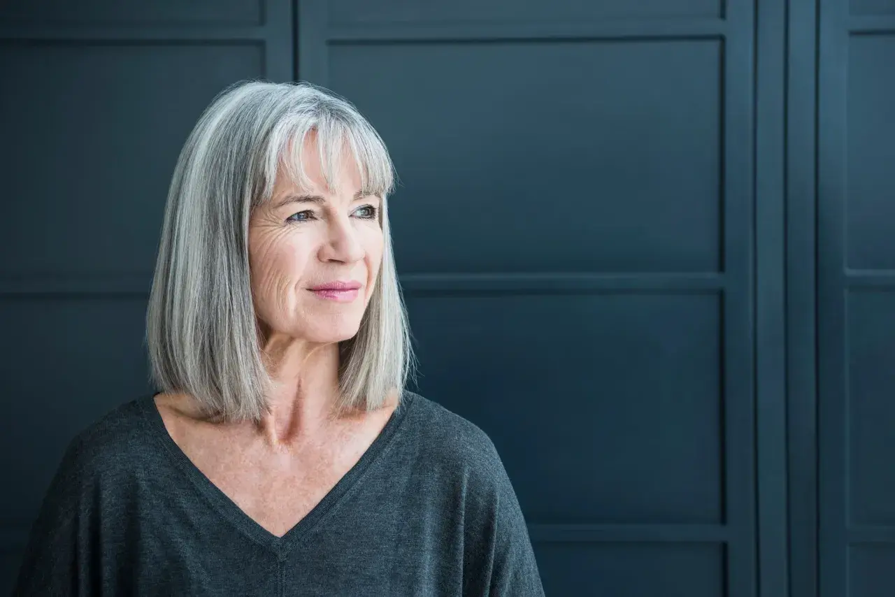 Een vrouw met grijs haar kijkt peinzend weg. Ze straalt een rustige kracht uit, wat kan passen bij de complexiteit van autisme bij vrouwen.