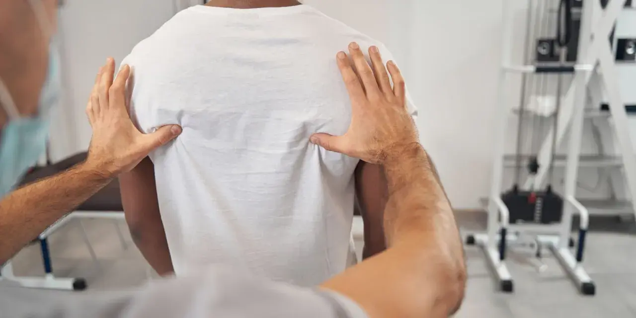 Fizjoterapeuta bada plecy pacjenta, szukając przyczyn bólu żeber, który może być związany ze zwyrodnieniem kręgosłupa.