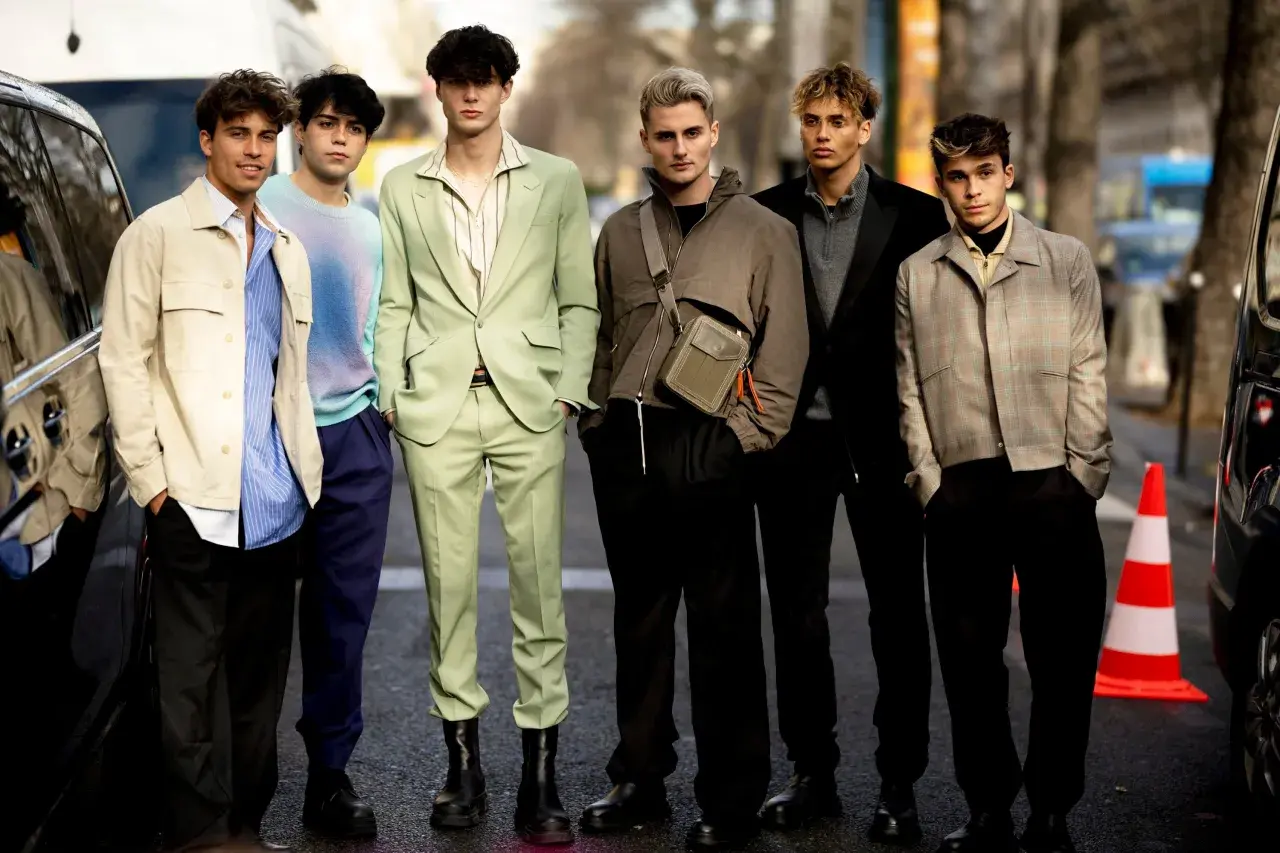 Sechs junge Männer präsentieren modische Outfits. Einer trägt einen schwarzen Blazer, der elegant zu kombinieren ist.