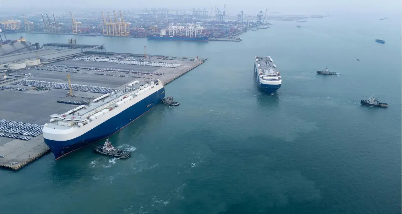 Große Autotransporter im Hafen, bereit für den Roll-on/Roll-off-Verkehr. Schlepper assistieren beim Manövrieren.