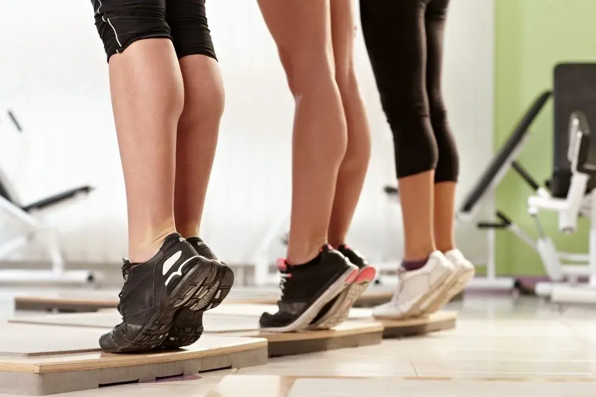 Tre donne eseguono un **calf raise** in palestra, sollevando i talloni per allenare i polpacci.