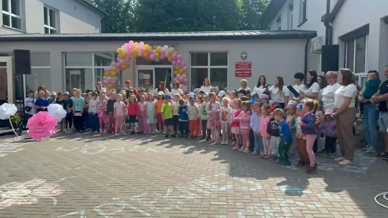 Dzieci i dorośli stoją przed budynkiem ozdobionym balonami. Widać biała podlaska atrakcje dla dzieci, takie jak wielkie papierowe kwiaty i rysunki na chodniku.