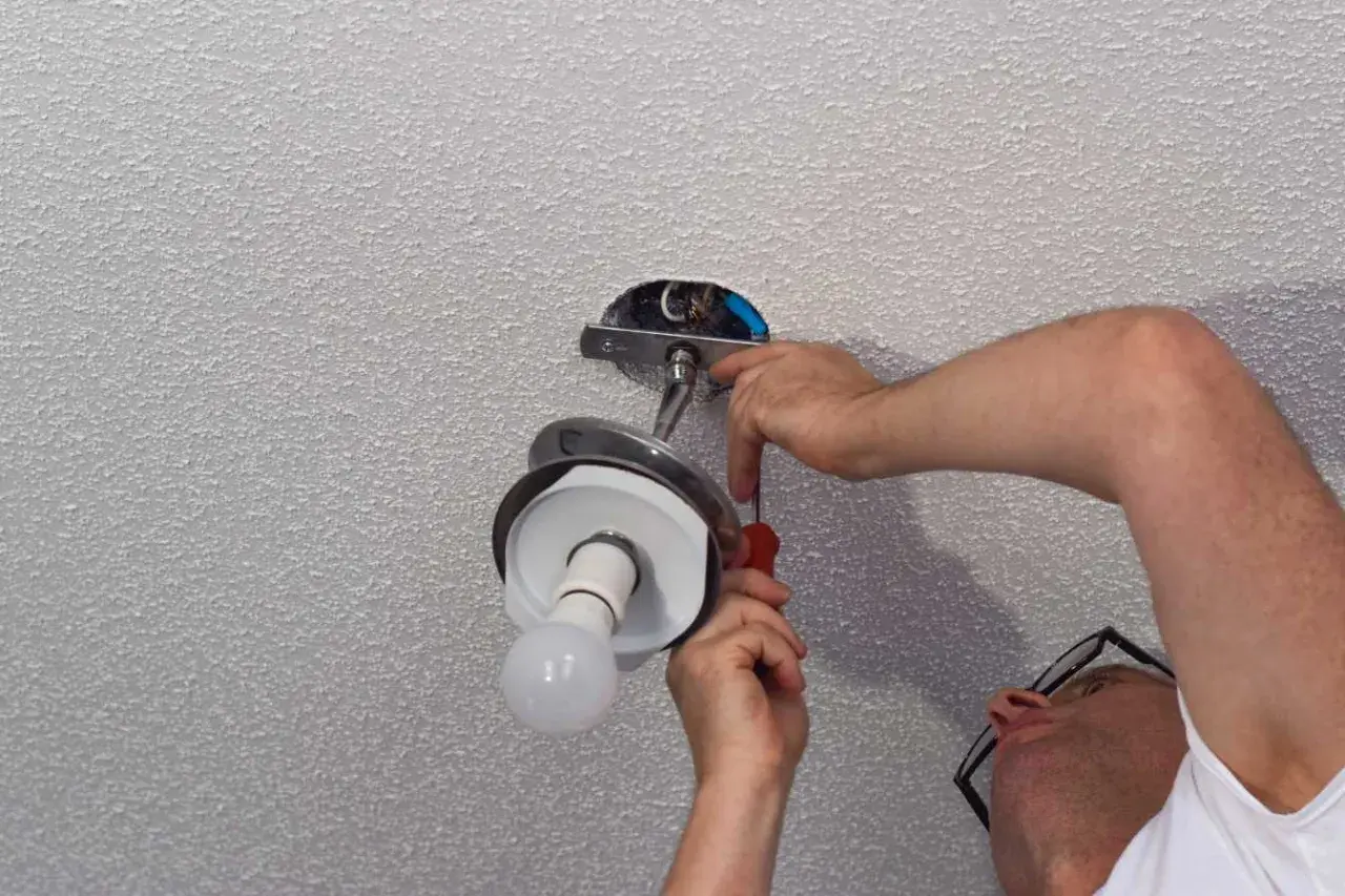 Un homme effectue le branchement d'une lampe au plafond, utilisant un tournevis pour fixer le luminaire.