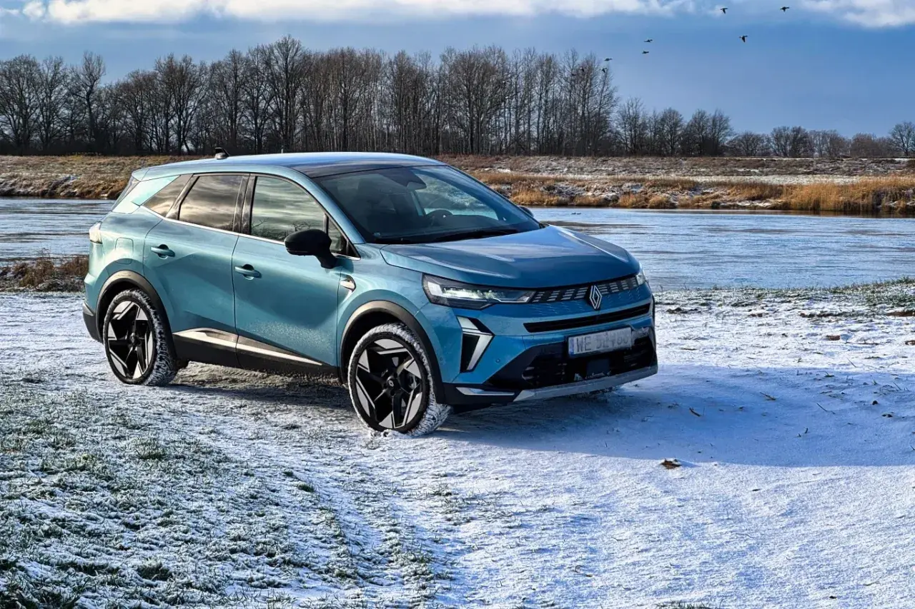 Niebieski Renault Symbioz zaparkowany na zaśnieżonej polanie nad zamarzniętą rzeką.